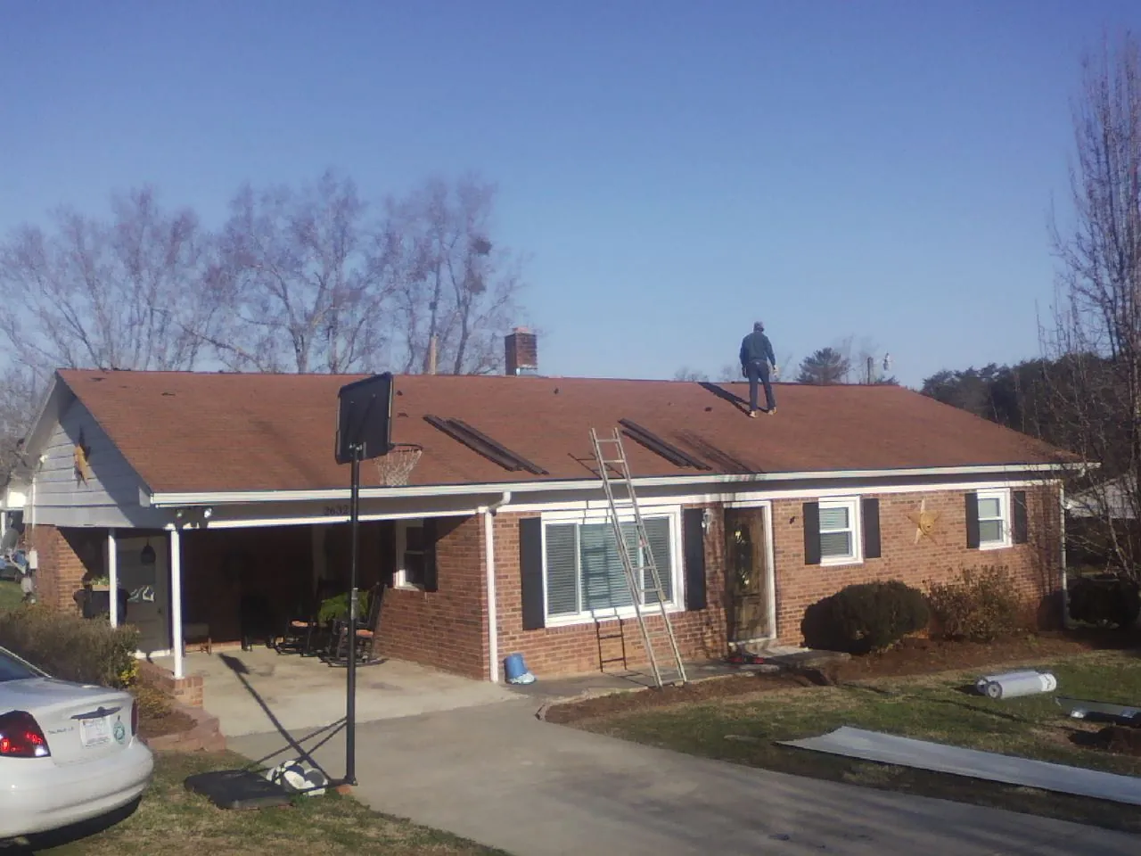 Roofer stripping a shingle roof on a brick ranch before metal panels in Bayville