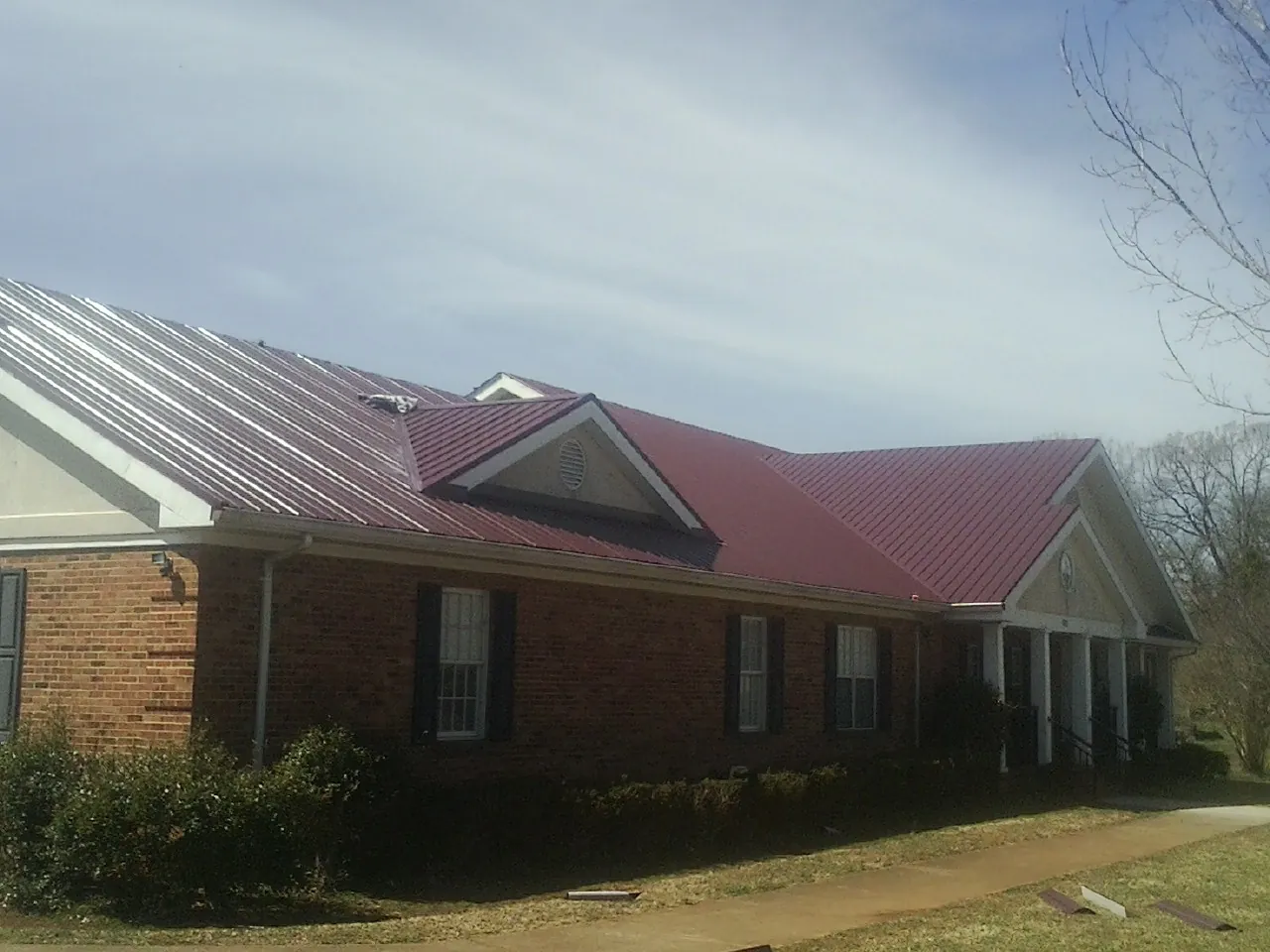 Red metal roof with gabled entries on a long brick building, from a Hail Damage Roof Repair job in Bayville